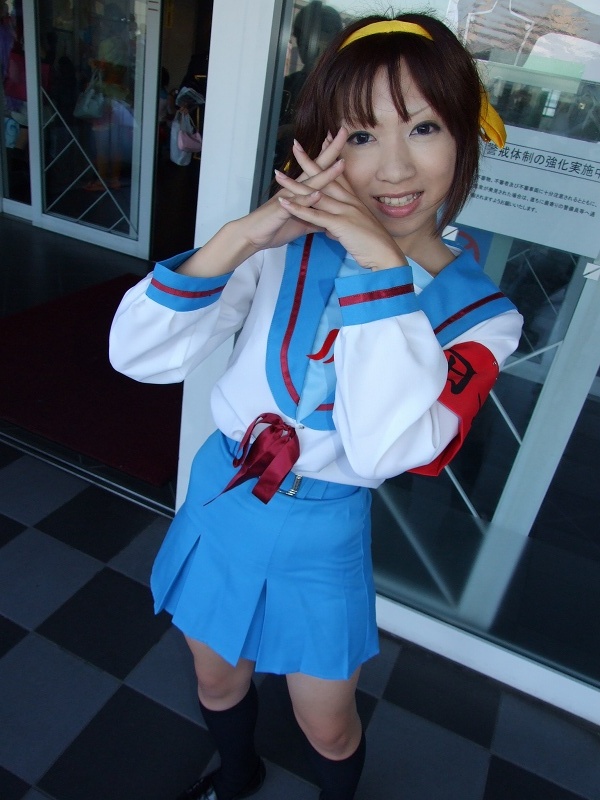 torai aki, suzumiya haruhi, suzumiya haruhi no yuuutsu, photo (medium), 1girl, armband, asian, cosplay, female focus, hair ribbon, kneehighs, looking at viewer, outdoors, ribbon, sailor, school uniform, serafuku, socks, solo, suzumiya haruhi (cosplay)