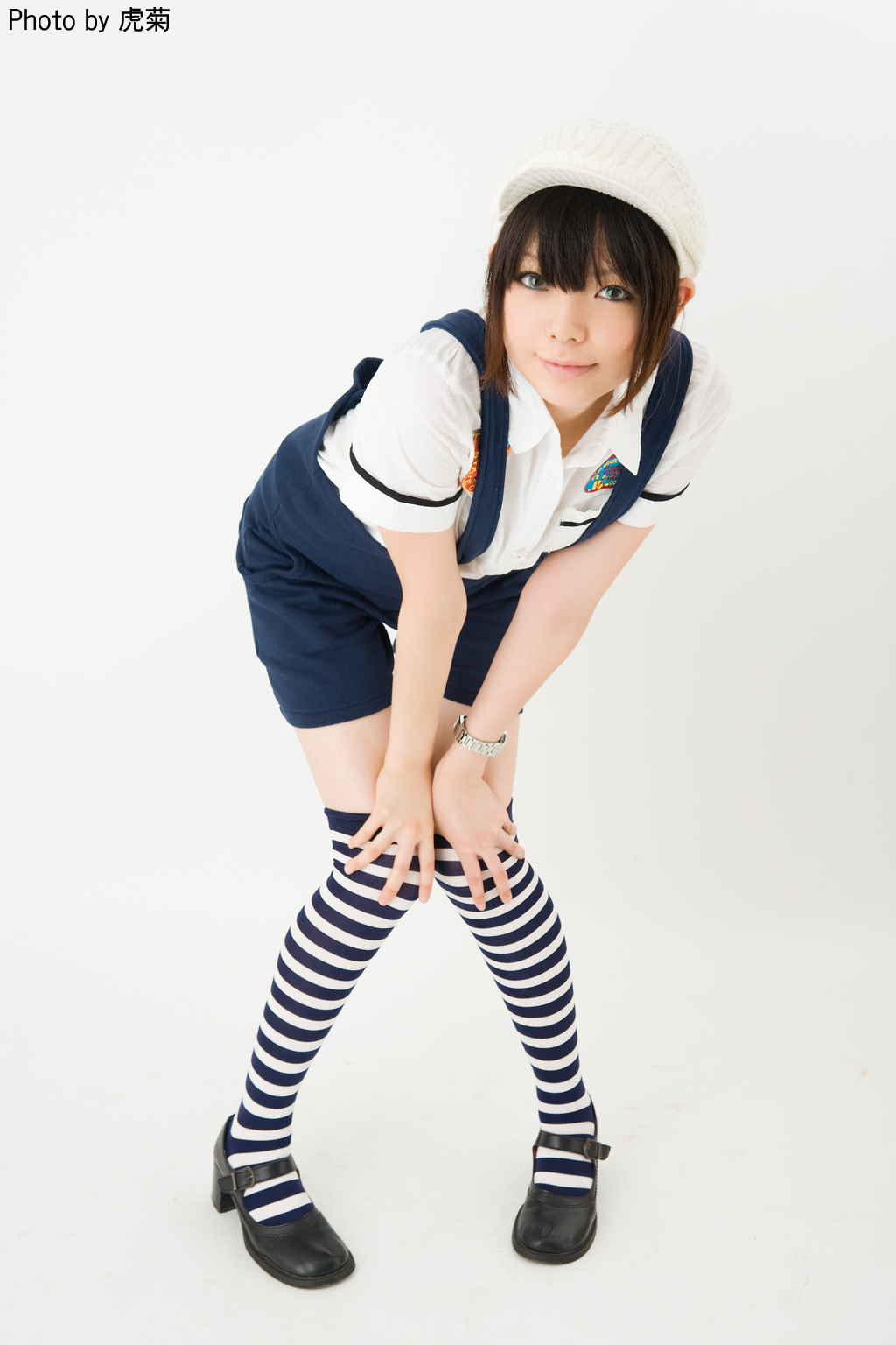 namada, character request, cosplay request, highres, photo (medium), 1girl, artist name, asian, black shoes, blue eyes, blue overalls, brown hair, color contacts, female focus, full body, hands on own knees, hat, knees together feet apart, leaning forward, looking at viewer, mary janes, overall shorts, overalls, pigeon-toed, shoes, short sleeves, shorts, simple background, solo, standing, striped clothes, striped thighhighs, thighhighs, watch, white background, white hat, wristwatch, zettai ryouiki