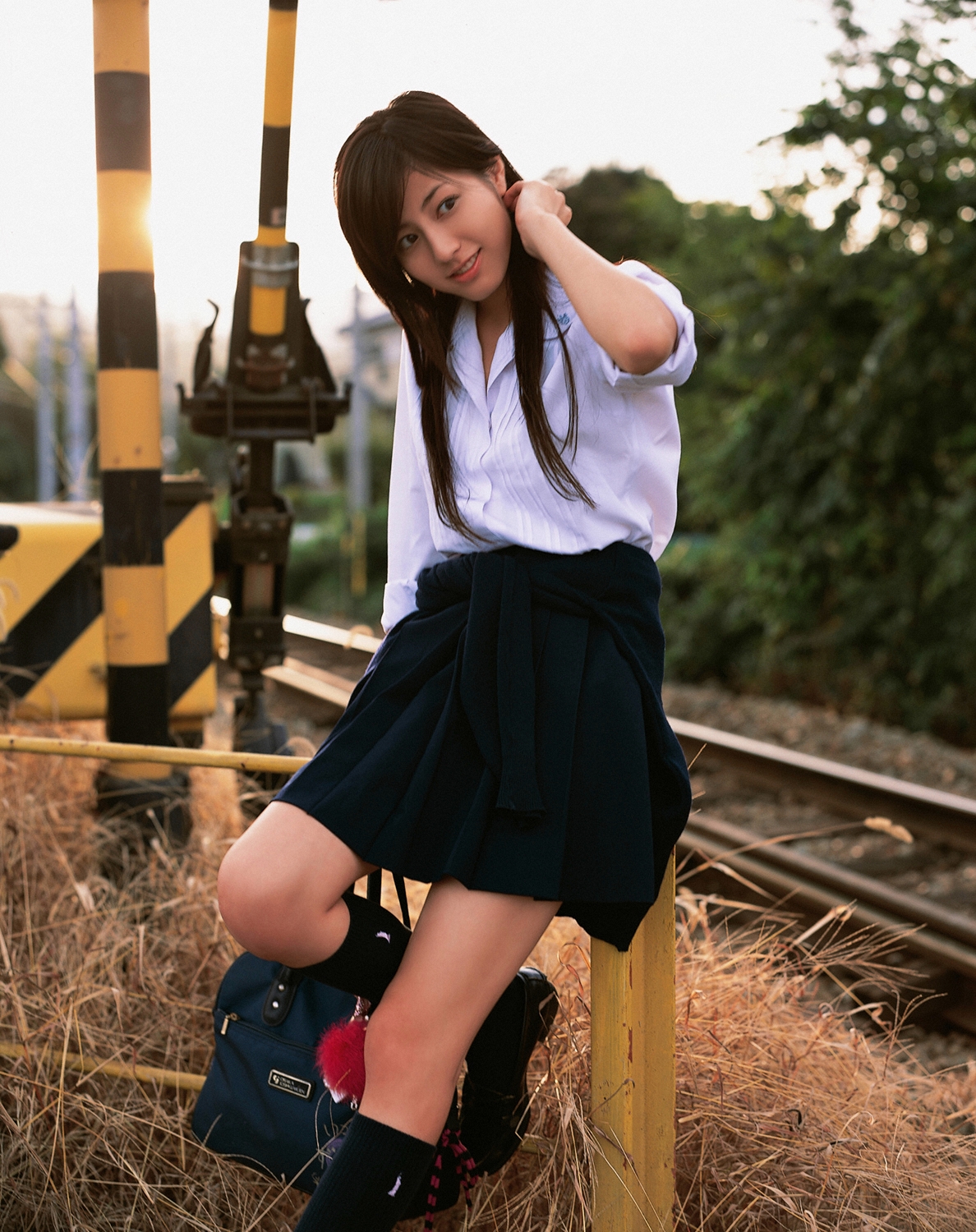 sugimoto yumi, highres, photo (medium), 1girl, asian, bag, brown hair, cosplay, female focus, kneehighs, long hair, looking at viewer, miniskirt, pleated skirt, railroad crossing, railroad tracks, school bag, school uniform, skirt, socks, solo, standing