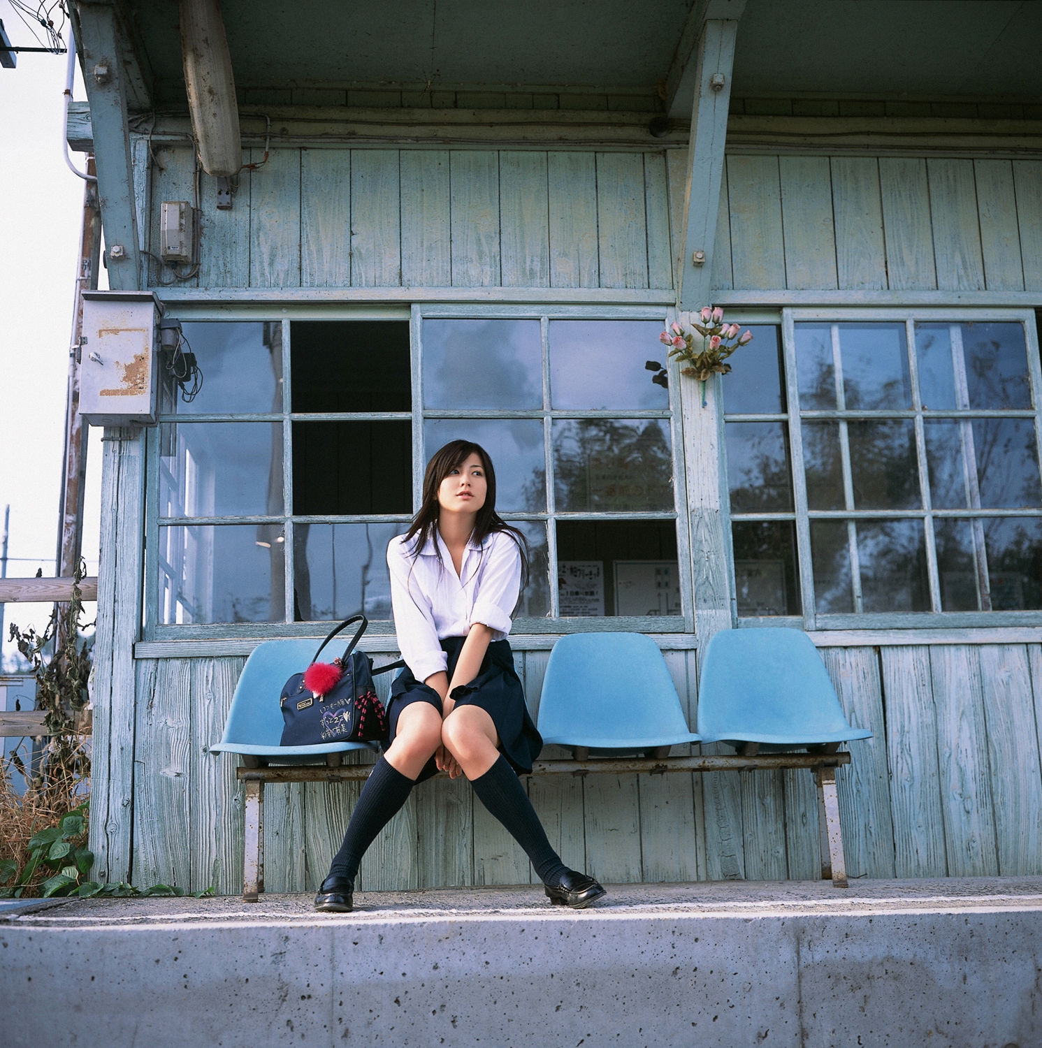 sugimoto yumi, highres, photo (medium), 1girl, asian, bag, brown hair, cosplay, female focus, kneehighs, knees together feet apart, long hair, looking at viewer, miniskirt, pleated skirt, railroad tracks, school bag, school uniform, sitting, skirt, socks, solo, train station