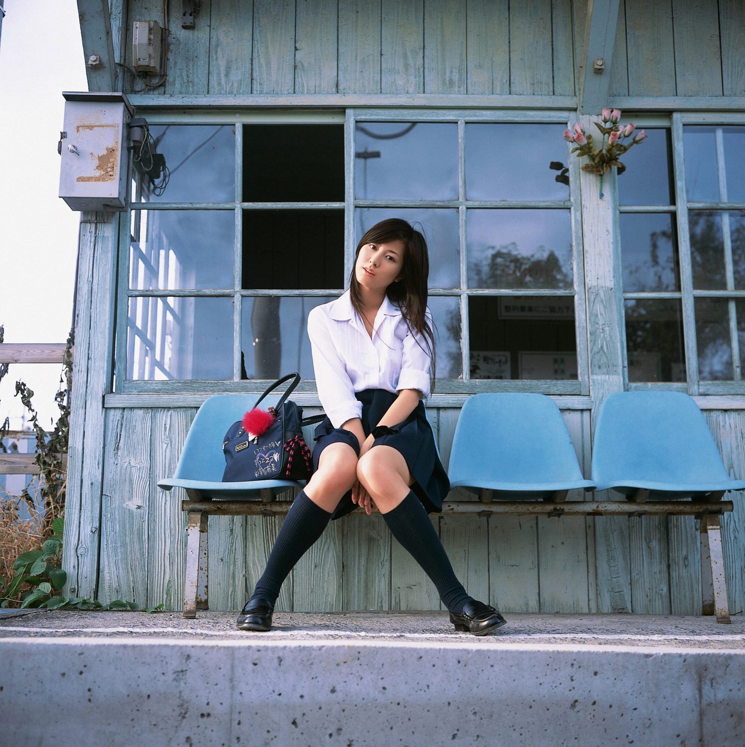 sugimoto yumi, highres, photo (medium), 1girl, asian, bag, brown hair, cosplay, female focus, kneehighs, knees together feet apart, long hair, looking at viewer, miniskirt, pleated skirt, railroad tracks, school bag, school uniform, sitting, skirt, socks, solo, train station