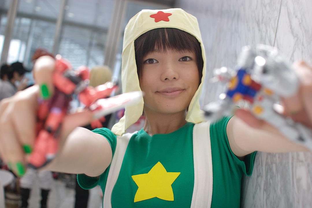 namada, keroro, gundam, keroro gunsou, photo (medium), 1girl, action figure, asian, black hair, blurry, breasts, cosplay, depth of field, dutch angle, female focus, green nails, green shirt, gunpla, happy, indoors, keroro (cosplay), looking at viewer, model kit, nail polish, outstretched arms, shirt, short sleeves, small breasts, smile, solo, standing, star (symbol), suspenders, t-shirt, toy