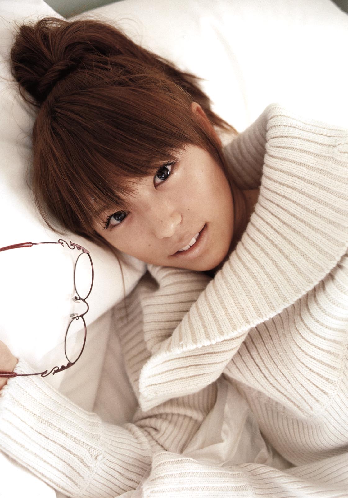 wakatasuki chinatsu, highres, photo (medium), tagme, 1girl, asian, brown hair, female focus, freckles, glasses, indoors, japanese (nationality), looking at viewer, lying, on side, parted lips, pillow, ponytail, solo, sweater, unworn eyewear, white sweater