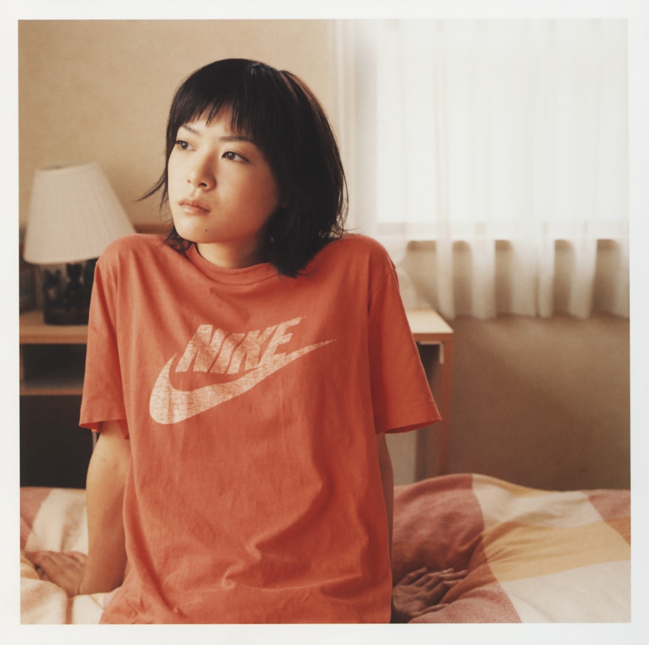 ueno juri, a piacere, nike (company), looking away, highres, photo (medium), 1girl, arm support, asian, bed, bedroom, border, female focus, indoors, japanese (nationality), looking to the side, shirt, solo, t-shirt, white border