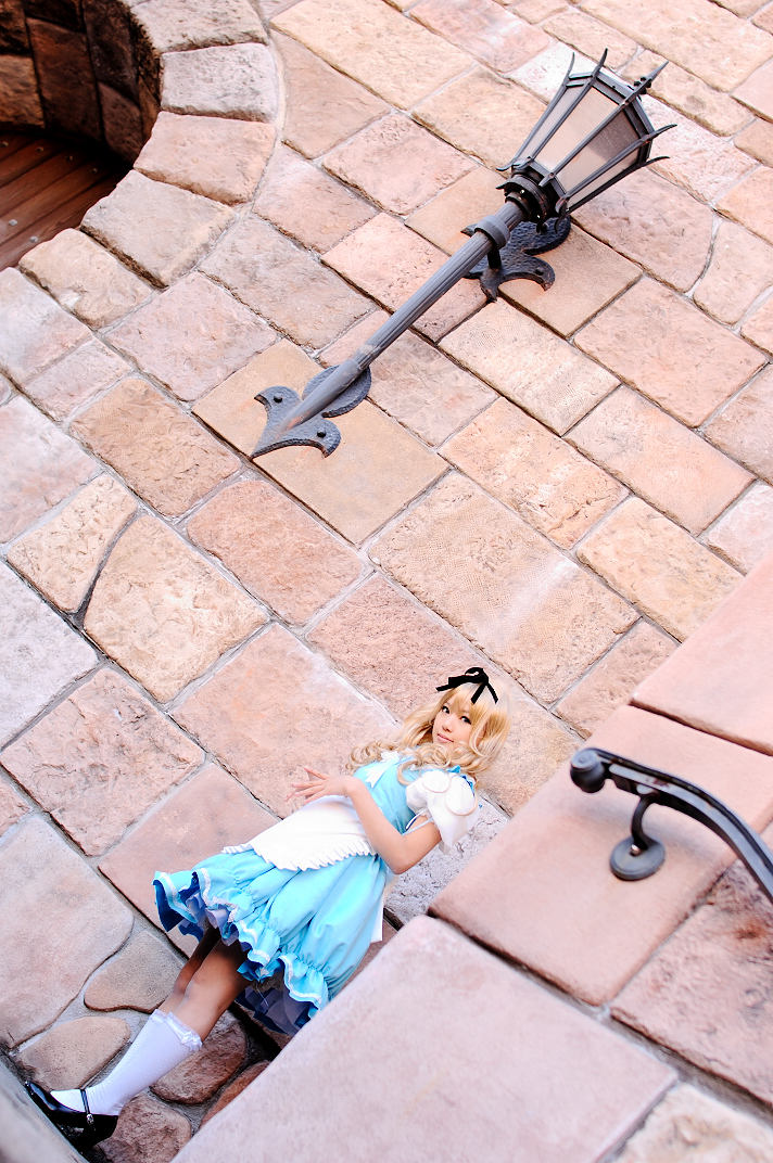 kipi-san, alice (alice in wonderland), alice's adventures in wonderland, photo (medium), 1girl, alice (alice in wonderland) (cosplay), apron, asian, blonde hair, breasts, cosplay, dutch angle, female focus, hair ribbon, kneehighs, long hair, looking at viewer, outdoors, petite, ribbon, small breasts, socks, solo