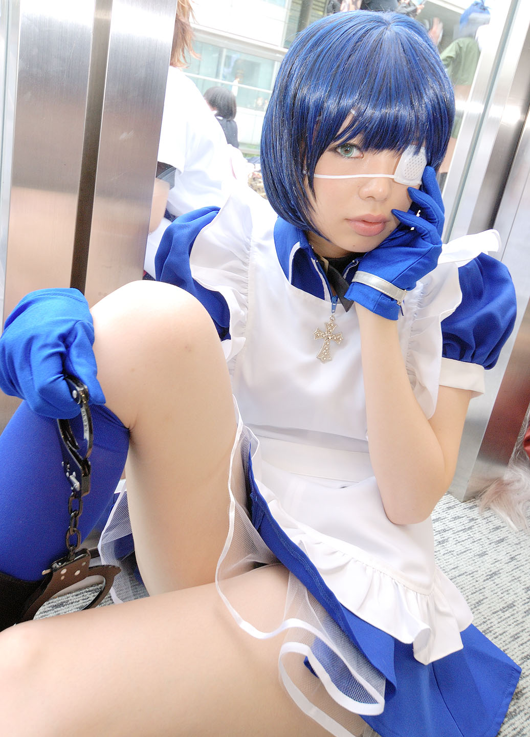 namada, ryomou shimei, ikkitousen, highres, photo (medium), 1girl, apron, asian, blue eyes, blue gloves, blue hair, blue socks, boots, collar, color contacts, cosplay, cross, cuffs, dutch angle, eyepatch, female focus, gloves, handcuffs, indoors, kneehighs, looking at viewer, maid, maid apron, on floor, puffy short sleeves, puffy sleeves, ryomou shimei (cosplay), short sleeves, sitting, socks, solo