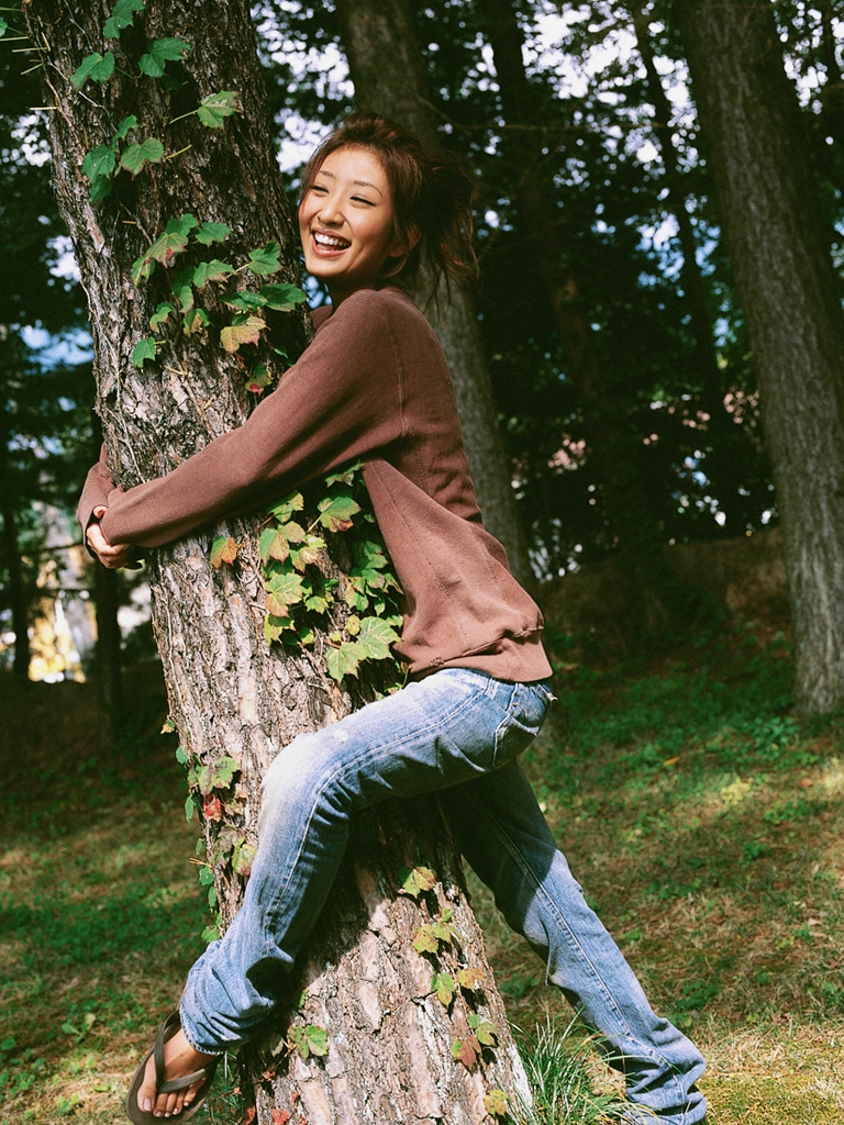 ando sayaka, photo (medium), 1girl, against tree, asian, brown hair, dendrophilia, denim, dutch angle, dyed hair, female focus, forest, grass, high ponytail, ivy, jeans, nature, outdoors, pants, ponytail, sandals, short hair, smile, solo, sweater, tree, tree hug