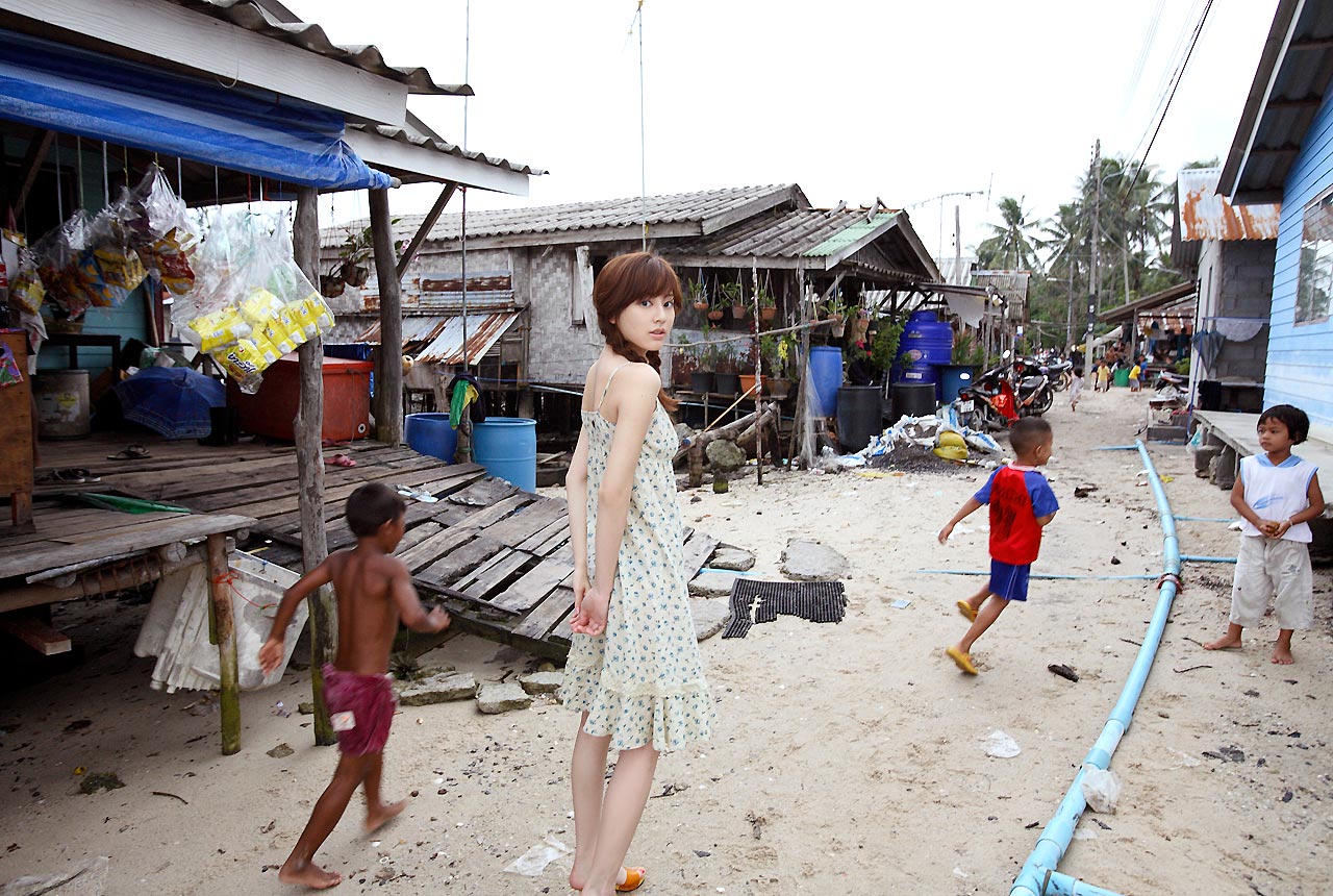 sugimoto yumi, rosebud, photo (medium), 1girl, 3boys, asian, braid, brown hair, dark-skinned male, dark skin, dress, full body, japanese (nationality), long hair, looking at viewer, looking back, multiple boys, outdoors, standing, sundress, twin braids