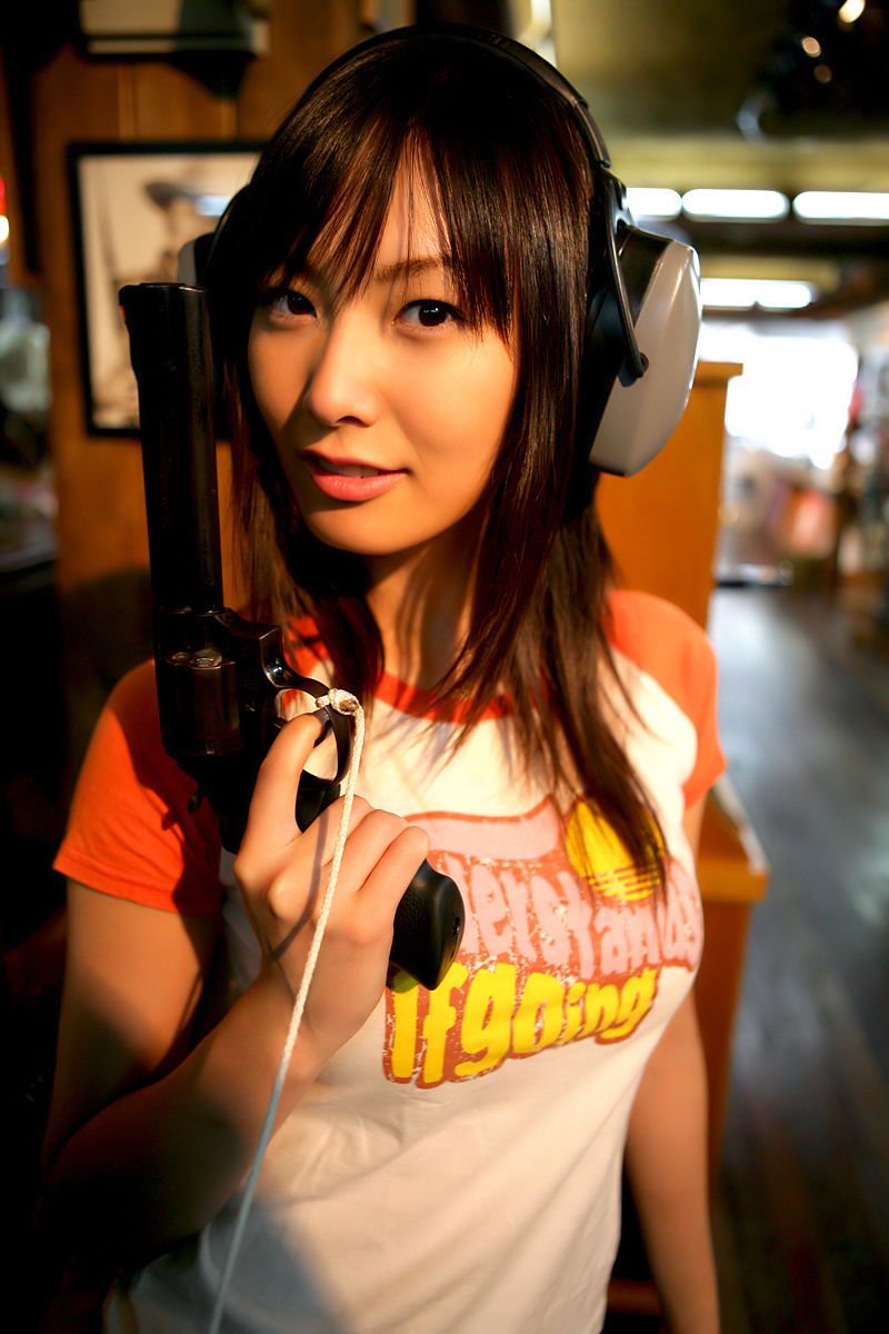 nagasawa nao, nao mail, highres, photo (medium), 1girl, asian, breasts, brown hair, female focus, gun, indoors, light smile, long sleeves, looking at viewer, parted lips, raglan sleeves, shirt, short sleeves, smile, solo, t-shirt, upper body, weapon