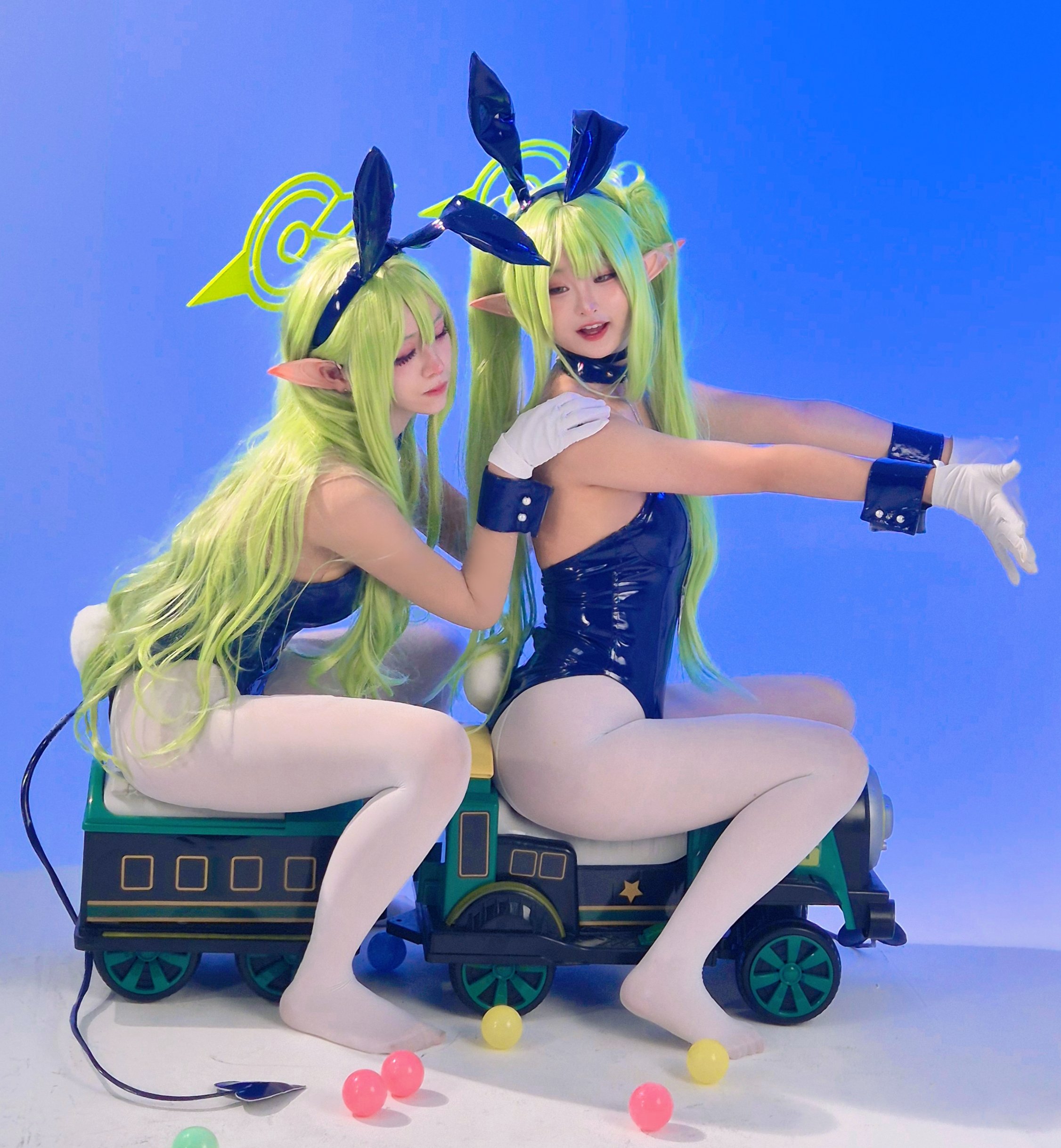 hikari (blue archive), nozomi (blue archive), blue archive, real life, photo (medium), 2girls, ball, blue background, blue leotard, breasts, choker, closed eyes, collar, cosplay, cuffs, demon tail, gloves, green hair, hand on another's shoulder, leotard, multiple girls, pantyhose, playboy bunny, pointy ears, ponytail, rabbit ears, rabbit tail, sitting, spade tail, spiked collar, spikes, tail, toy train, train, twintails, white pantyhose