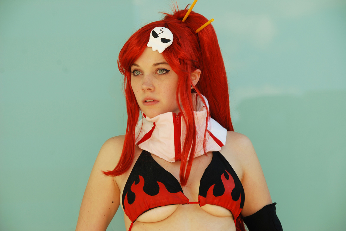 ellarcy, yoko littner, tengen toppa gurren lagann, cosplay photo, photo (medium), 1girl, bikini, bikini top only, breasts, cleavage, cosplay, earrings, elbow gloves, female focus, gloves, green eyes, jewelry, large breasts, nose stud, ponytail, red hair, skull, solo, stud earrings, swimsuit, underboob, wig