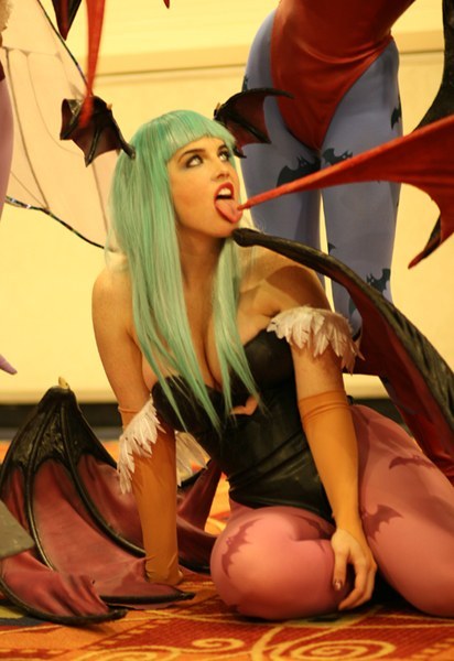 lilith (darkstalkers), lindze, morrigan aensland, capcom, darkstalkers, print legwear, cosplay photo, photo (medium), 2girls, animal print, bat print, breasts, cosplay, demon girl, elbow gloves, gloves, green hair, head wings, large breasts, leotard, licking, lilith (darkstalkers) (cosplay), lipstick, long hair, makeup, morrigan aensland (cosplay), multiple girls, pantyhose, red leotard, sitting, tongue, wings