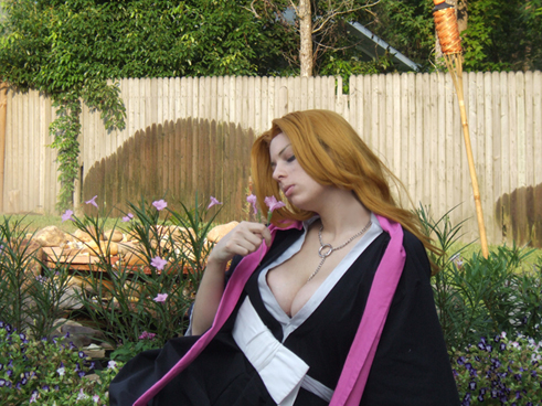 dani'elle, matsumoto rangiku, bleach, cosplay photo, lowres, photo (medium), 1girl, breasts, cleavage, closed eyes, cosplay, female focus, fence, flower, jewelry, large breasts, long hair, necklace, orange hair, solo