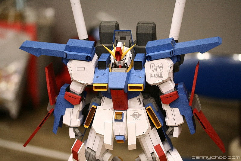 danny choo, zz gundam, gundam, gundam zz, papercraft (medium), photo (medium), unconventional media, arms at sides, blurry, blurry background, clenched hands, cowboy shot, figure (medium), mecha, no humans, robot, standing, watermark, web address