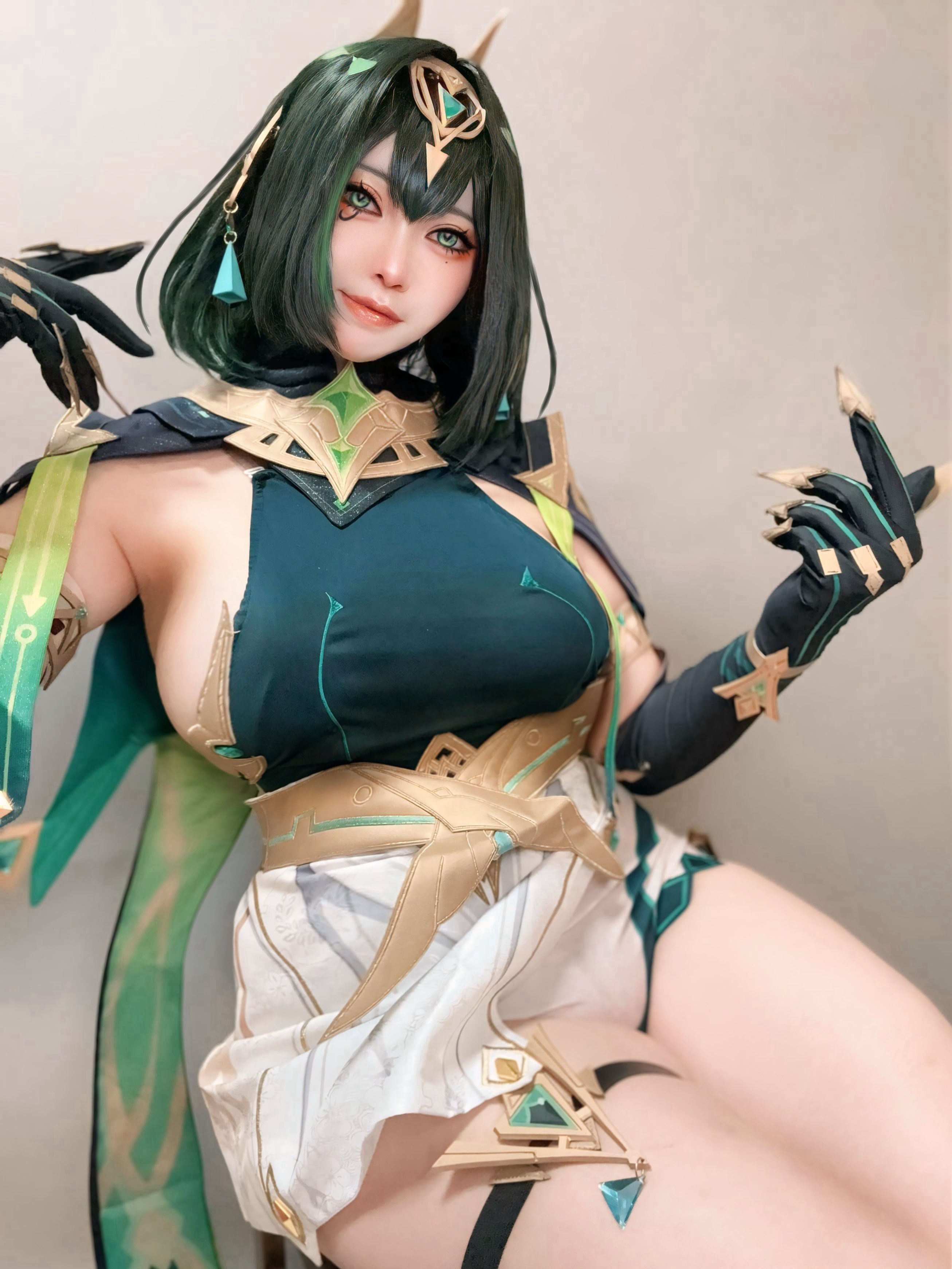 nueyama nueccha, nefer (genshin impact), genshin impact, absurdres, cosplay photo, highres, photo (medium), 1girl, ancient egyptian clothes, armpit crease, breasts, closed mouth, earpiece, elbow gloves, eye tattoo, fake claws, gloves, green eyes, green hair, green shirt, large breasts, looking at viewer, medium hair, mole, mole under eye, shirt, sitting, skirt, solo, tattoo, thigh strap, usekh collar, white skirt