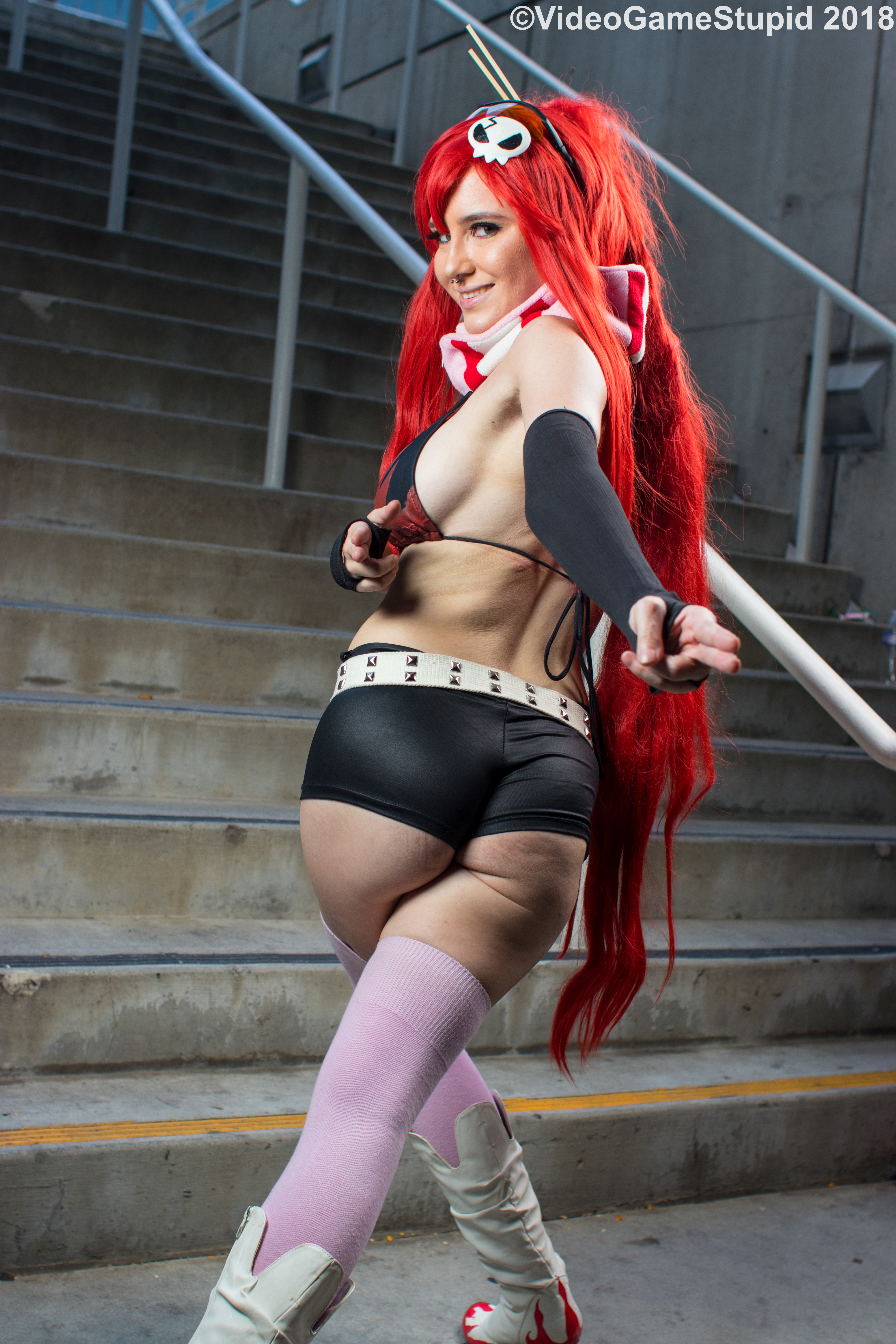 beccadex, yoko littner, real life, tengen toppa gurren lagann, cosplay photo, photo (medium), 1girl, ass, asymmetrical gloves, belt, bikini, bikini top only, breasts, cleavage, elbow gloves, fingerless gloves, flame print, gloves, hair ornament, hair stick, high ponytail, large breasts, leather shorts, long sidelocks, looking at viewer, navel, no shirt, nose piercing, nose ring, piercing, pink scarf, pink thighhighs, ponytail, red hair, scarf, short shorts, shorts, sidelocks, single elbow glove, skull hair ornament, solo, stairs, stairwell, studded belt, sunglasses, thighhighs, uneven gloves, yoko littner (cosplay)