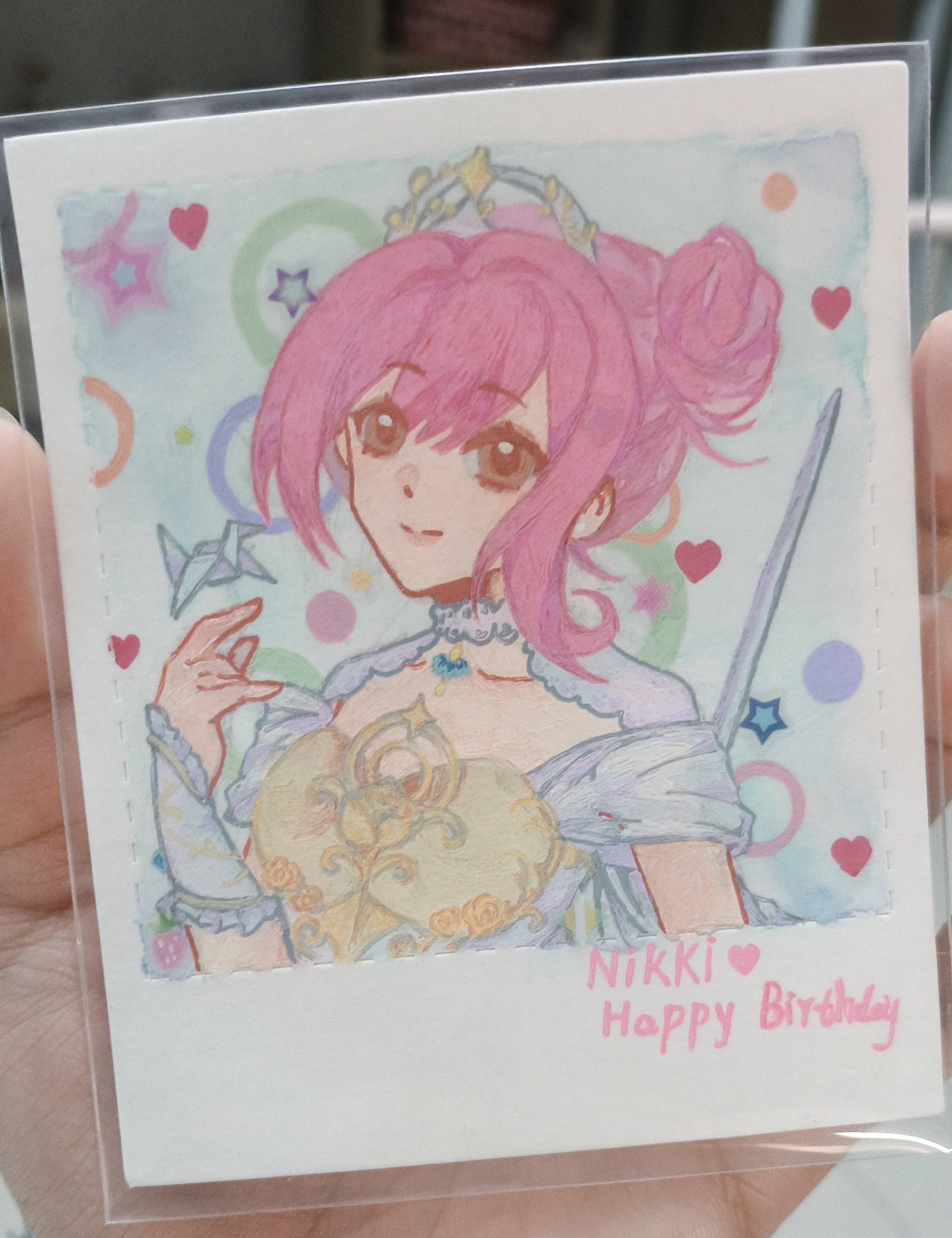 melody bloom (infinity nikki), nikki (nikki), infinity nikki, nikki (series), absurdres, highres, painting (medium), photo (medium), traditional media, 1girl, armor, artist's hand in frame, blue background, blue gemstone, breastplate, brooch, brown eyes, character name, chest jewel, closed mouth, collar, collarbone, detached collar, dot nose, dress, english text, eyelashes, gem, hair between eyes, hair bun, hand up, happy, happy birthday, heart, heart brooch, jewelry, lace collar, lips, looking at viewer, object floating above hand, off-shoulder dress, off shoulder, origami, paper crane, pink hair, pink lips, polka dot, polka dot background, short hair with long locks, short sleeves, single side bun, single sidelock, smile, solo, star (symbol), sue78218, sword, sword on back, tiara, updo, upper body, weapon, weapon on back, white collar, white dress