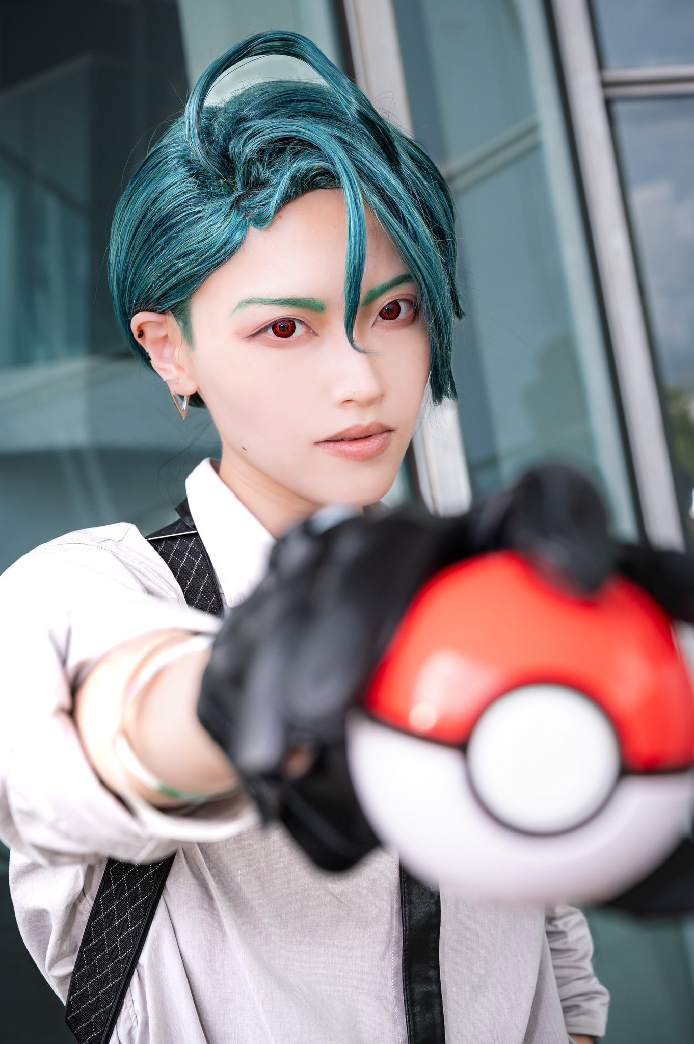 nintendo, pokemon, pokemon sv, real life, commentary, cosplay photo, highres, photo (medium), 1girl, 2025, androgynous, arm at side, asian, black gloves, blurry, blurry background, blurry foreground, building, collared shirt, cosplay, cowlick, earrings, female focus, foreshortening, gloves, holding, holding poke ball, japanese (nationality), jewelry, kazuki isshiki (cos11p), lips, long sleeves, outdoors, parted lips, perspective, poke ball, poke ball (basic), reaching, reaching towards viewer, red eyes, reflection, reverse trap, shirt, solo, suspenders, upper body, v-shaped eyebrows, white shirt