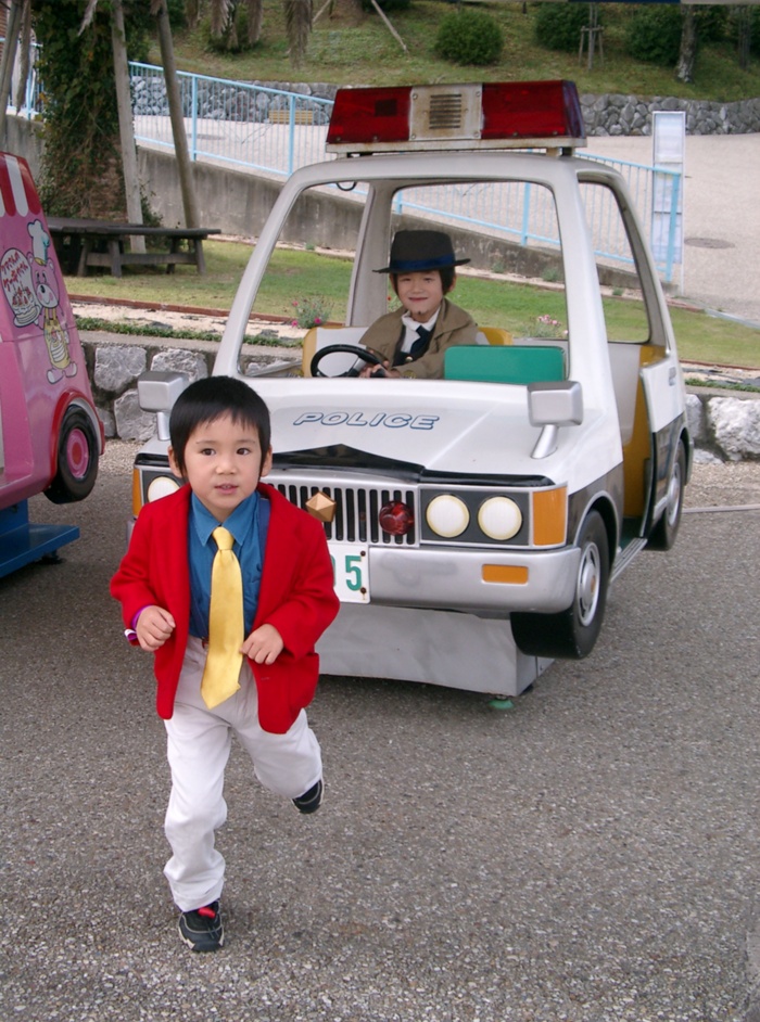 arsene lupin iii, zenigata kouichi, lupin iii, black neckwear, vehicle, yellow neckwear, photo (medium), 2boys, car, chasing, child, cosplay, hat, jacket, motor vehicle, multiple boys, necktie, police car, red jacket, running